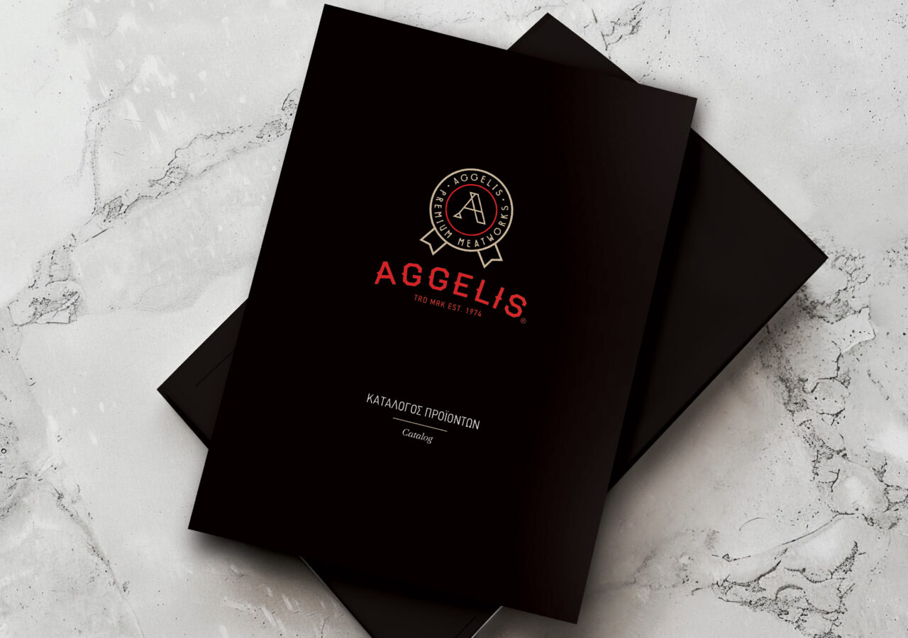 Aggelis Meatworks Product Catalog με μαύρο φόντο, χρυσό λογότυπο και κόκκινα γράμματα, τοποθετημένος σε μαρμάρινη επιφάνεια.